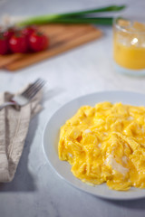 Soft scrambled eggs plain next to fork, napkin, tomatoes, orange juice and green onions