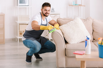 Male janitor cleaning furniture in room