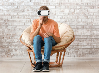 Young man with VR glasses sitting near brick wall