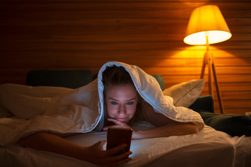 Young beautiful woman in bed using mobile phone late at night at dark bedroom lying happy and relaxed enjoying social media network at her phone in communication internet addiction concept