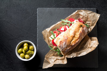 Sandwich with jamon, cheese, tomatoes and arugula on a black background
