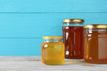 Jars with different types of organic honey on wooden table against light blue background. Space for text