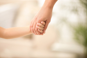 Mother holding hands with her child indoors, closeup. Happy family