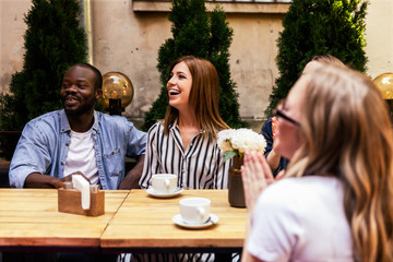 African boy and caucasian girls are laughing at the cosy open air cafe at the hot sunny day