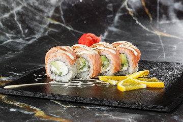 Sushi Rolls with flamed salmon, cucumber and Cream Cheese inside on black slate isolated on black...