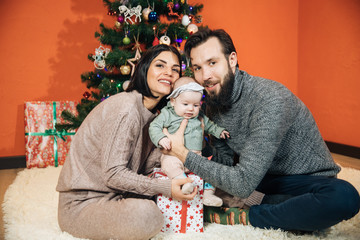 young family with a child near the Christmas tree, mom dad and their newborn daughter prepare for the New Year and Christmas, happy family