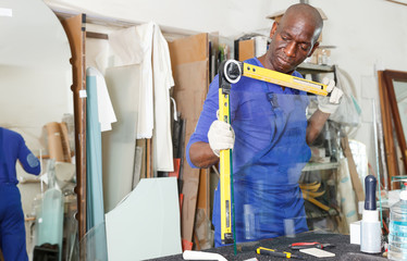 professional African American glazier using multifunction angle finder level for measuring glass size