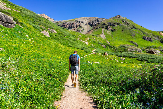 Man hiker walking through open green meadow field summit on trail to Ice lake near Silverton, Colorado in August 2019 summer sunny day