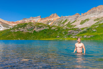 Young happy fit man standing swimming in cold colorful water of Ice Lake on famous trail in Silverton, Colorado in San Juan Mountains in summer