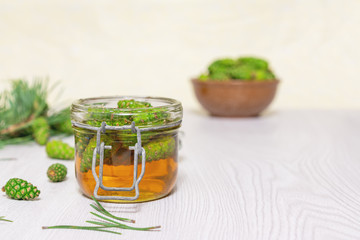 Honey and young green pine cones in an open glass jar on a light wooden table. Gourmet dessert. Natural medicine