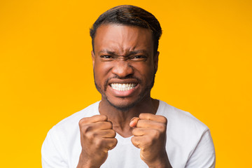 African American Guy Clenching Fists Looking At Camera, Yellow Background
