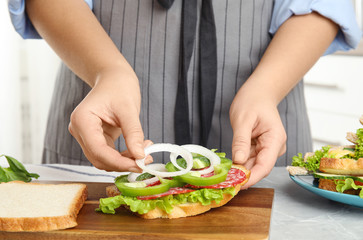 Woman adding onion to tasty sandwich at light grey marble table, closeup
