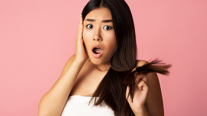 Shocked asian girl showing dry edges of damaged hair