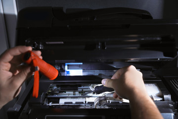 Repairman with flashlight fixing modern printer indoors, closeup