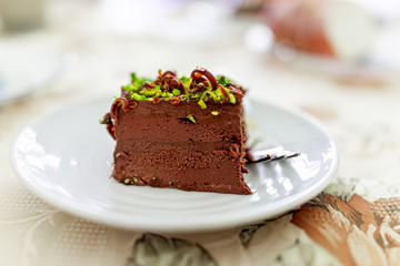 Fototapeta na wymiar Closeup of homemade layered pistachio dark chocolate raw vegan cake slice on white plate with chocolate shavings and nut green pieces texture