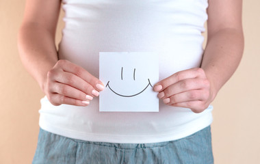 A close-up view of the belly of a pregnant woman in a white T-shirt that is holding a piece of...