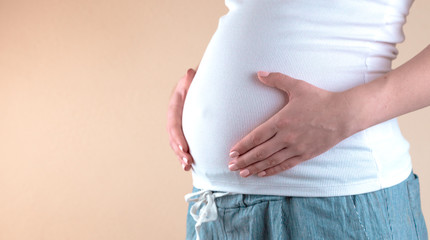 Authentic close up shot of an young pregnant woman in pajamas is caressing her belly just woke up in a bedroom in the morning.