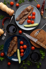 Healthy paleo or keto food. Roasted meat with raw tomatoes and cucumbers served with red wine on black background