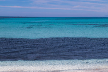 Multi coloured water and sky of Spiaggia le Saline, white pebble beach in Stintino, Sardinia, Italy.