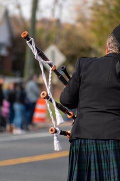 Scottish bagpipe player in full uniform playing the bagpipes during a Veterans Day parade. Musician is seen in traditional Scottish tartan attire. Photo taken in vertical, portrait orientation. 