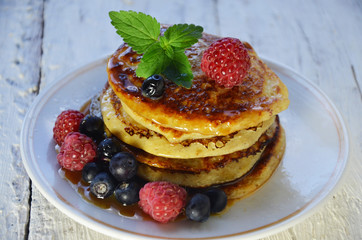 Pancakes with berries and maple syrup in a plate on a white wooden background