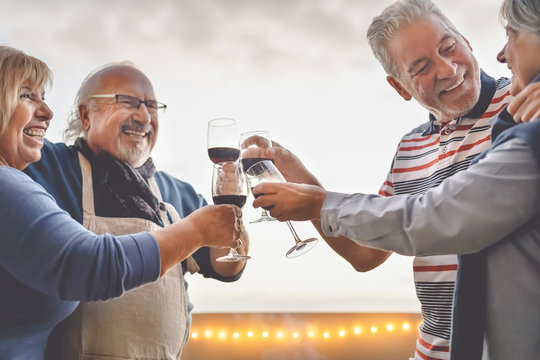 Happy seniors friends drinking red wine on terrace sunset - Mature people having fun laughing and sharing time together outdoor - Elderly retirement lifestyle activity  concept
