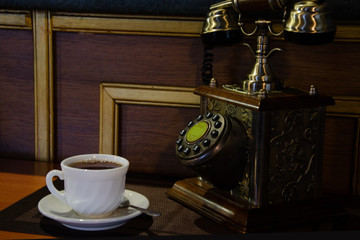 Fototapeta na wymiar Retro telephone and white cup with a hot drink on a coffee table.