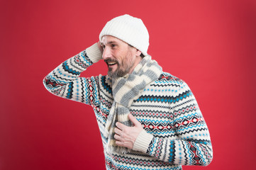 So cozy. Winter collection. Mature man enjoy warmth comfort. Cold winter conditions. Handsome bearded guy wearing hat scarf red background. Winter sweater. Knitted accessories. Winter weather style