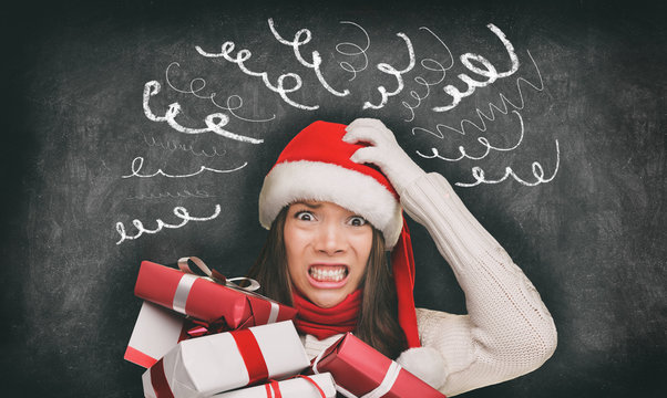 Christmas stress winter holiday shopping gifts woman in santa hat stressed out funny drawings of headache spirals on black blackboard banner panorama. Anxious shopper late for family gifts.