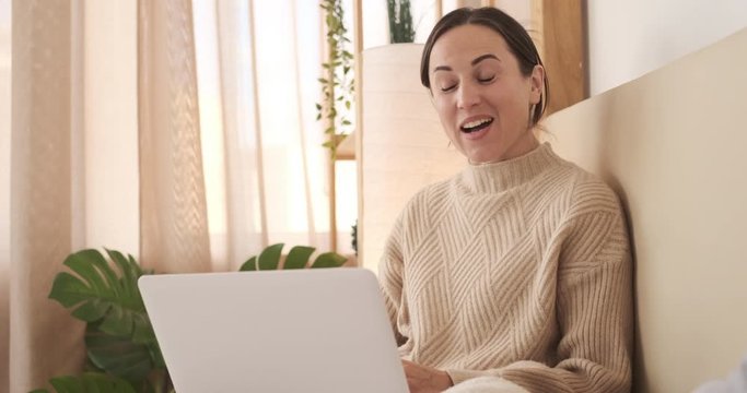 Happy woman making a video call using laptop on bed at home