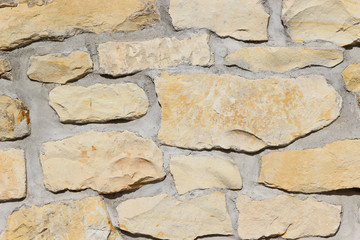 Wall made of natural rocks of different sizes and shapes with wide gaps filled with cement 