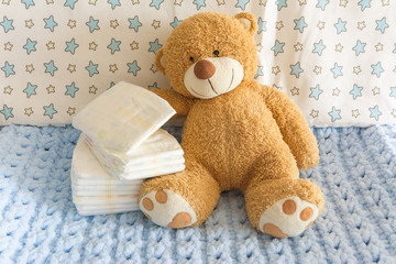 diapers with baby soft toy bear on the background of the nursery and crib, the concept of using...