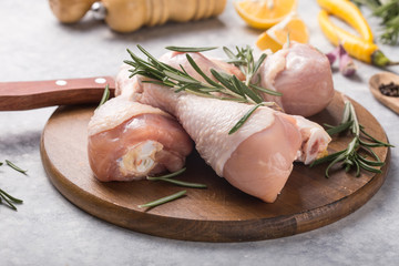 Raw organic uncooked chicken legs or drumsticks on round wooden board with ingredients for cooking (pepper, lemon, rosemary, salt, garlic). Meat top view