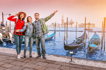 Fototapeta na wymiar Happy three friends hugging in Venice near sea channel with gondolas boats