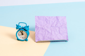 Mini size alarm clock beside a Paper sheet placed tilted on pastel backdrop