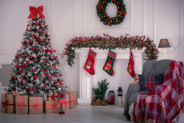 Modern living room with Christmas decorations in evening: white fir tree decorated with red balls,...