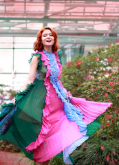 Fototapeta premium beautiful red-haired girl in arranger where azalea blooms in a colorful flying dress
