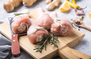 Raw organic uncooked chicken legs or drumsticks on cutting board  with ingredients for cooking (pepper, lemon, rosemary, salt, garlic). Meat top view