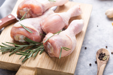 Raw organic uncooked chicken legs or drumsticks on cutting board  with ingredients for cooking (pepper, lemon, rosemary, salt, garlic). Meat top view