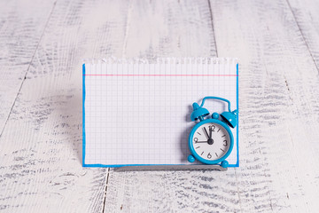 Mini blue alarm clock stand tilted above buffer wire in front of notepaper
