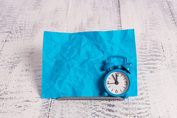 Mini blue alarm clock stand tilted above buffer wire in front of notepaper