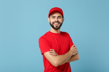 Delivery man in red uniform workwear isolated on blue wall background, studio portrait. Professional male employee in cap t-shirt print working as courier dealer. Service concept. Mock up copy space.