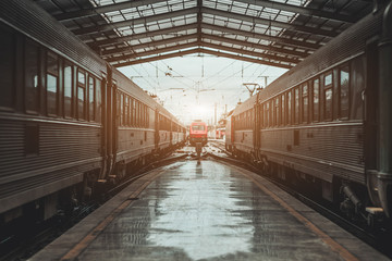 Obraz na płótnie Canvas Symmetrical view of a railroad station depot with a triangle roof above, a modern red locomotive being in a defocused background on maintenance, two high-speed trains on both sides of the platform