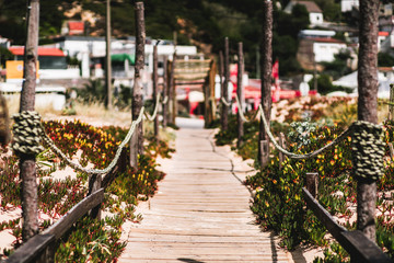 Fototapeta na wymiar A long wooden outdoor passageway in a warm summer resort from the beach to the inner area: wooden fence, rope tied between pillars, shallow depth of field with a selective focus on the foreground