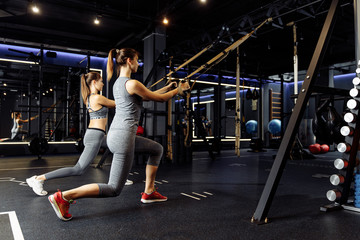 Two athletes woman with arms raised train with elastic bands in gym