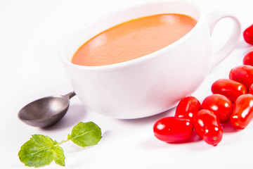 Gazpacho soup decorated with fresh mint and some tomatoes on a white background with a vintage spoon