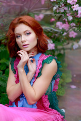 beautiful red-haired girl in arranger where azalea blooms in a colorful flying dress