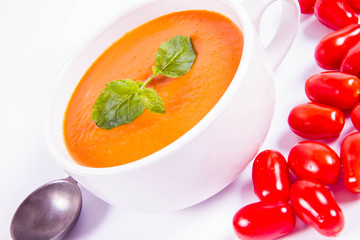 Gazpacho soup decorated with fresh mint and some tomatoes on a white background with a vintage spoon