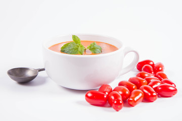 Gazpacho soup decorated with fresh mint and some tomatoes on a white background with a vintage spoon