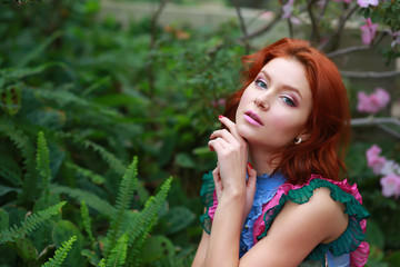 beautiful red-haired girl in arranger where azalea blooms in a colorful flying dress